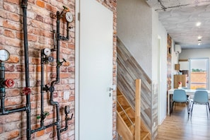 A modern interior with exposed brick walls, a wooden staircase, and a dining area with chairs.