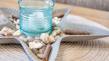 A glass container with a blue tint surrounded by various seashells and smooth stones on a textured surface.