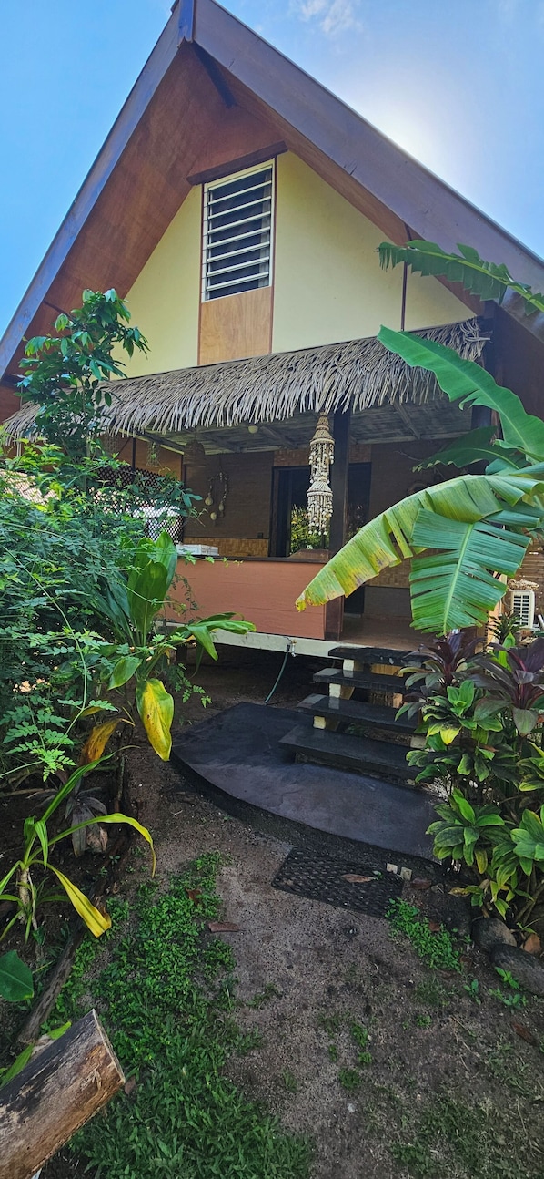 A house with a thatched roof, a small porch, and a staircase leading to the entrance.