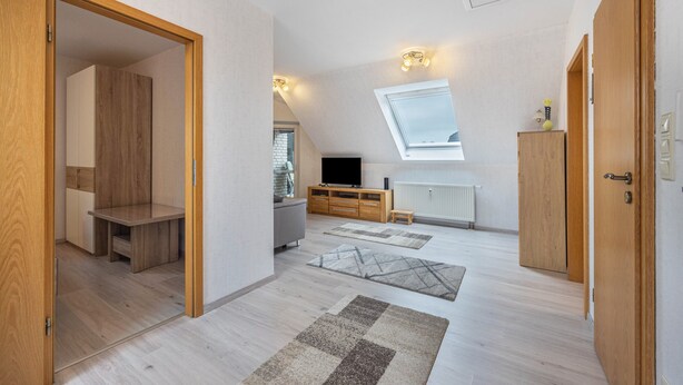 Ruime kamer met een vide, houten vloeren, een televisie en een dakraam.