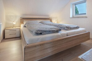 A bedroom with a wooden bed, bedside tables, a nightstand, a window, and a view of the outdoors. - Apartment 'Kastanie' with Balcony, Wi-Fi and Air Conditioning (Löhne)