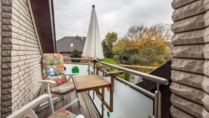 Een balkon met een houten tafel, stoelen en een witte parasol.