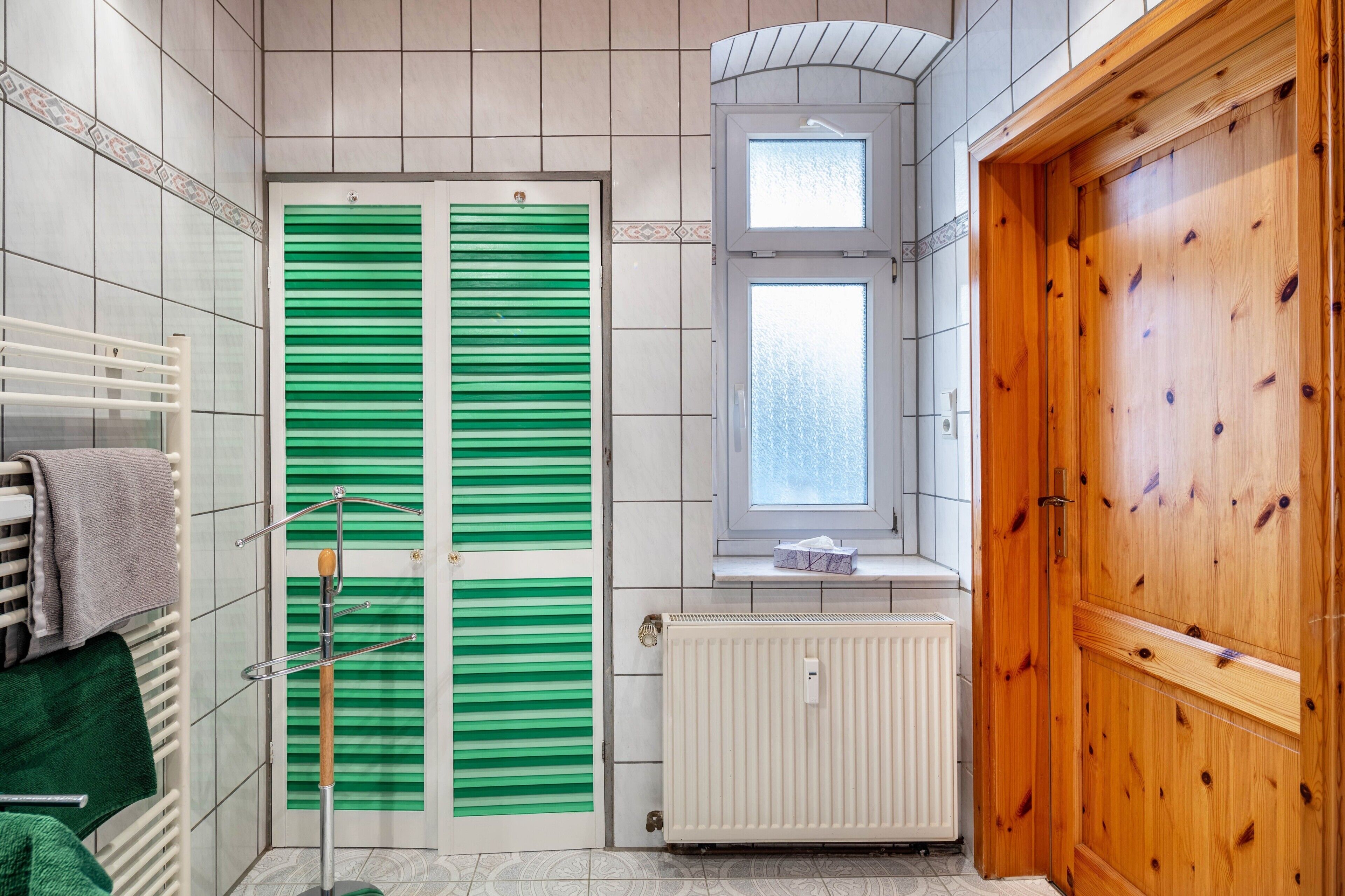 A bathroom with a green door, a white radiator, and a wooden door.