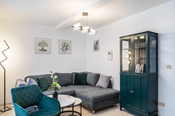 A modern living room with a sectional sofa, a teal armchair, a small round table, and a dark green cabinet.