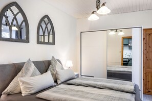 A bedroom with a bed, a nightstand, a lamp, a wardrobe, and two arched mirrors.