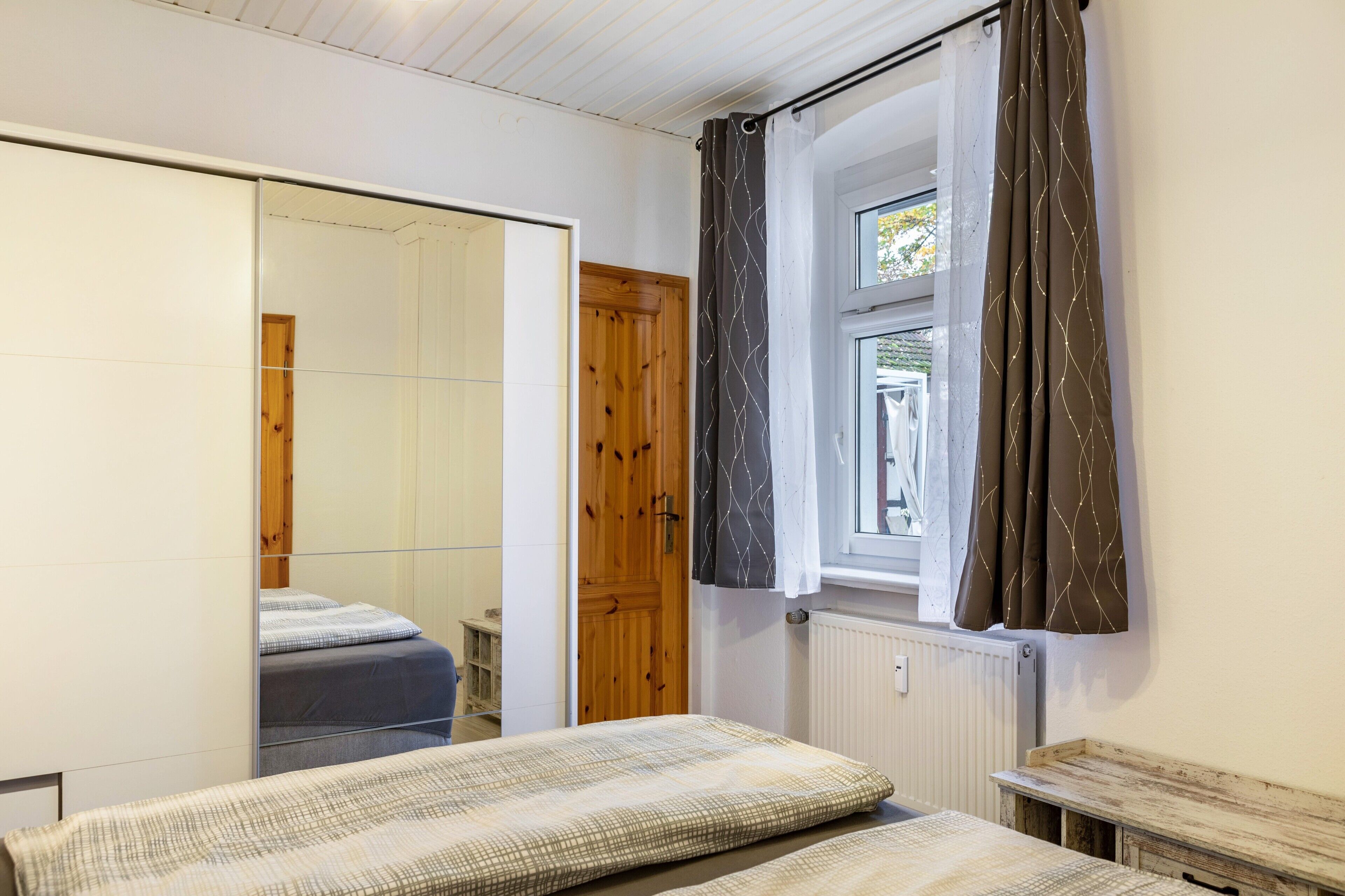 A bedroom with a bed, a wardrobe, a window with curtains, and a radiator.