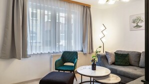 Moderni olohuone, jossa on vihreä nojatuoli, harmaa sohva, pyöreä sohvapöytä ja lattiavalaisin.