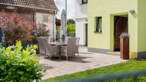 Eine Terrasse mit Korbmöbeln, einem Sonnenschirm und einer gelben Mülltonne.