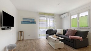A modern living room with a grey sofa, a coffee table, a television, and a small stool.