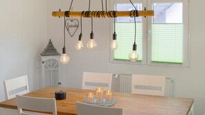 A dining area with a wooden table, white chairs, hanging light bulbs, and a small lantern.