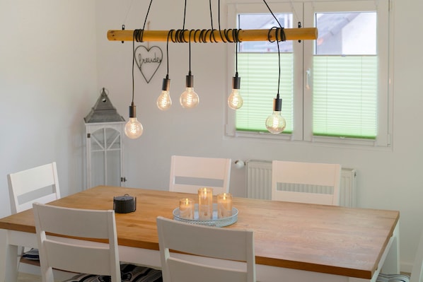 Un coin repas avec une table en bois, des chaises blanches, des ampoules suspendues et une petite lanterne.