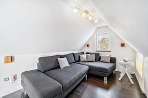 A modern loft with a gray sectional sofa, a small white side table, and a framed picture on the wall. - Apartment "Bayerl" with Mountain View, Balcony and Wi-Fi (Kirchseeon)