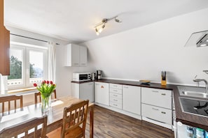A modern kitchen with white cabinets, a wooden dining table, and a view through the window. - Apartment "Bayerl" with Mountain View, Balcony and Wi-Fi (Kirchseeon)
