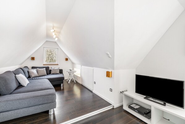 A modern loft bedroom with a large gray sectional sofa, a flat-screen TV, and a small white table.