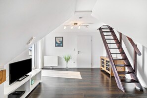 Un intérieur moderne avec un téléviseur posé sur une console blanche, une échelle en bois et une porte blanche.