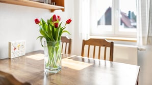 A dining table with a clear glass vase containing red tulips, a wooden chair, and a window with a view of buildings. - Apartment "Bayerl" with Mountain View, Balcony and Wi-Fi (Kirchseeon)