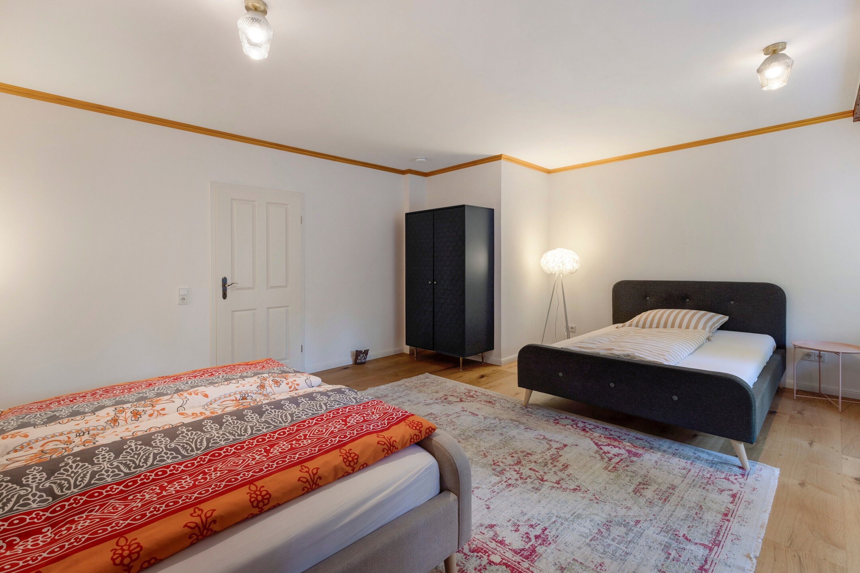A bedroom with two beds, a wardrobe, a bedside table, and a lamp.