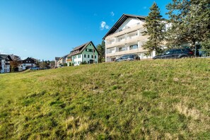 Un quartiere residenziale su una collina, con edifici a più piani, un prato in primo piano e un cielo azzurro intenso.