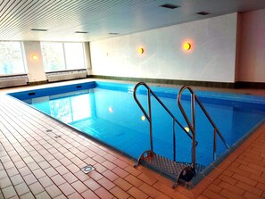 Una piscina interna con acqua cristallina, pareti piastrellate e pavimento piastrellato.