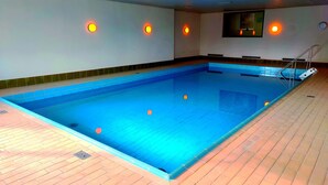 Ein Hallenbad mit Fliesenboden, einer Poolleiter und Wandleuchten.