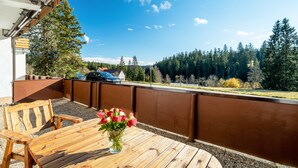 Ein Holztisch mit einem Blumenstrauß, eine Holzbank und Blick auf ein bewaldetes Gebiet.