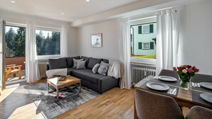 Ein modernes Wohnzimmer mit einer Couch, einem Couchtisch, einem Esstisch für zwei Personen und Blick ins Freie.
