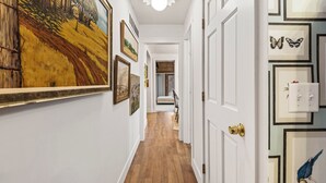 Un pasillo con piso de madera, paredes blancas y cuadros enmarcados.