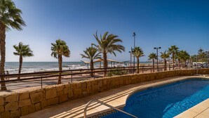 Une piscine bordée d’un mur en pierre, avec des palmiers et une vue sur la plage.