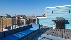 Una terraza con pared azul, una parrilla y mobiliario exterior.