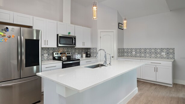 Una cocina moderna con armarios blancos, electrodomésticos de acero inoxidable, una isla central y un salpicadero decorativo.