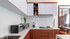 A modern kitchen with white subway tiles, wooden cabinets, a built-in microwave, and a gas stove. - Villa Blessing Bali (Ungasan)