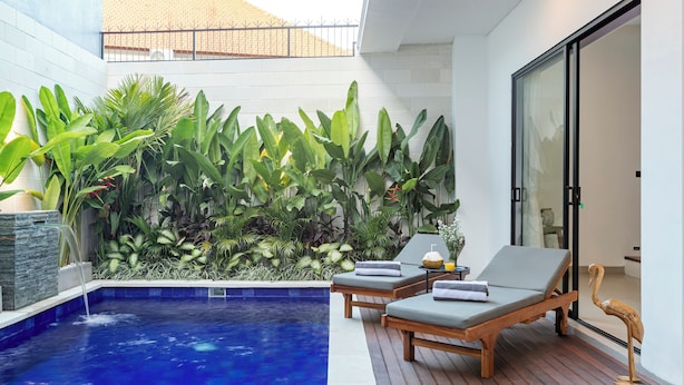 A modern outdoor pool area with lounge chairs and a variety of tropical plants. - Villa Blessing Bali (Ungasan)