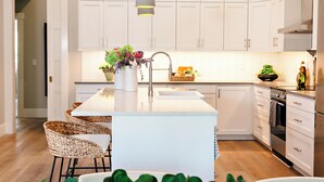 A modern kitchen with white cabinets, a central island with a sink, and a hanging pendant light.