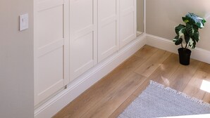 A room with a large white wardrobe, a potted plant, and a patterned rug on a wooden floor.