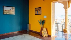 Vestíbulo de hotel con una pared azul, una pared amarilla y un piso de mármol. Hay un cuadro enmarcado en la pared azul y otro en la amarilla.