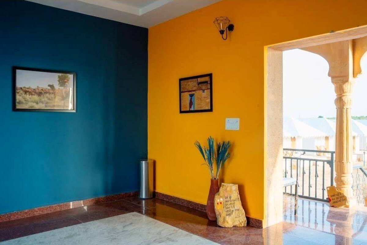 A hotel lobby with a blue wall, a yellow wall, and a marble floor. There is a framed picture on the blue wall and a framed picture on the yellow wall.