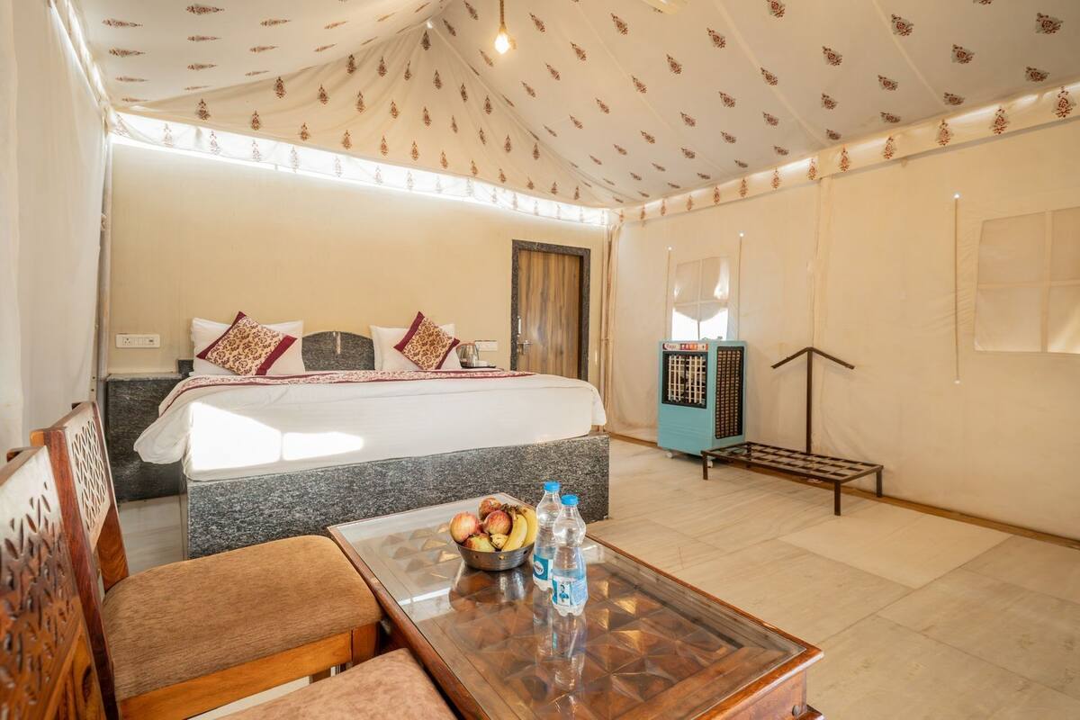 A hotel room with a bed, a dining table with fruits and water bottles, a heater, and a view of the outside.