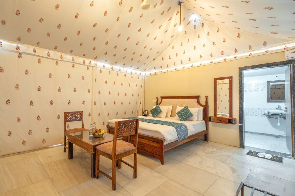 A bedroom with a bed, two chairs, a table with a bowl of fruit, and a shower area.