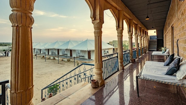 Un espacio al aire libre techado con un balcón, vista de carpas al fondo y una escalera que sube a un nivel superior.