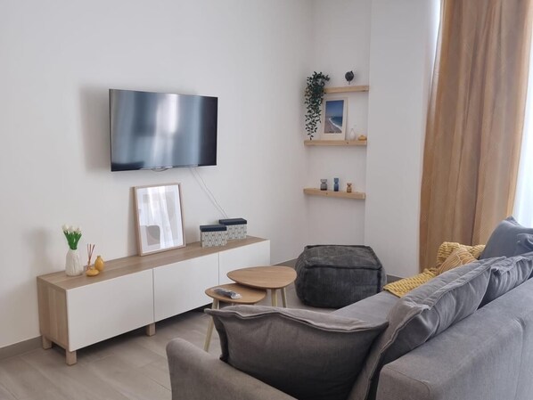 Una sala de estar moderna con una televisión de pantalla plana montada en la pared, un sofá, una mesita redonda y un banco.