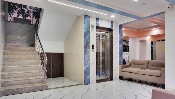 Un vestíbulo moderno con suelo de mármol, una escalera, un ascensor y un sofá color beige.