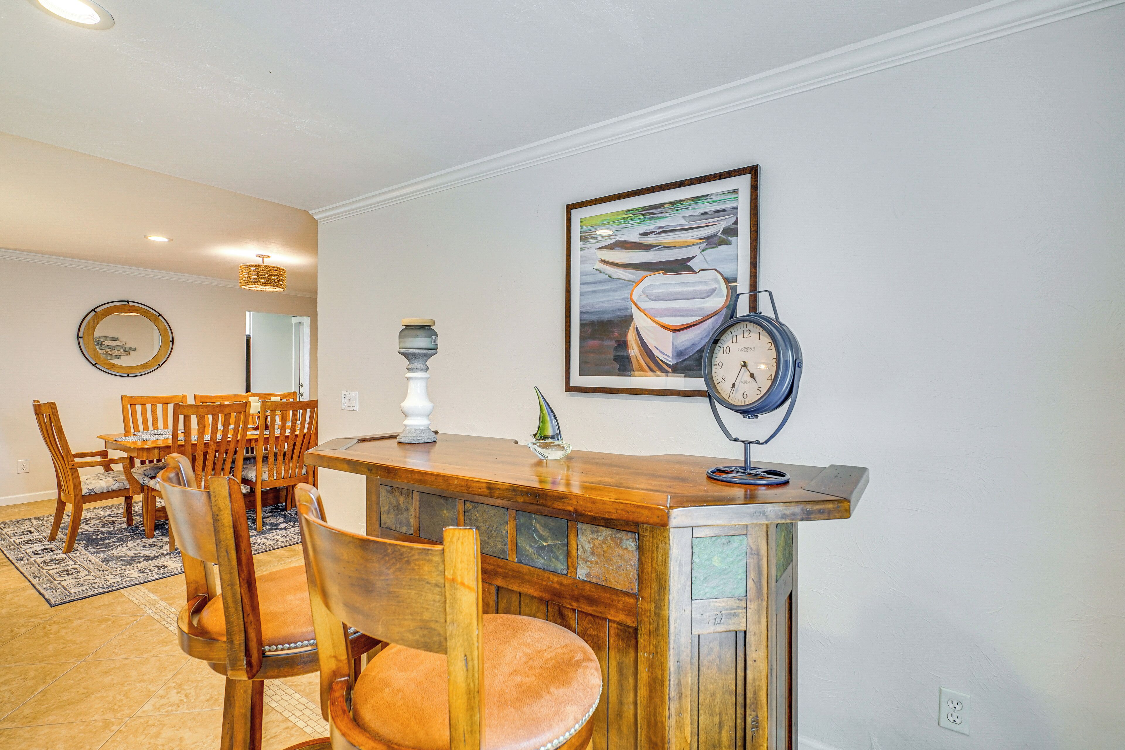 Un comedor con sillas de madera y una mesa, un reloj en la pared y un cuadro enmarcado sobre la mesa.