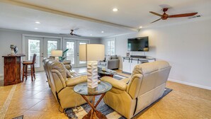 A spacious living room with a beige leather sofa, a glass coffee table, and a ceiling fan. - Canal-Front Home w/ Boat Lift in Cape Coral! (Cape Coral)