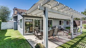 Een overdekt terras met tuinmeubilair, een pergola en uitzicht op de achtertuin.