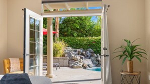 Une porte ouverte donne sur un patio agrémenté d’une cascade, d’une chaise et d’une plante en pot.