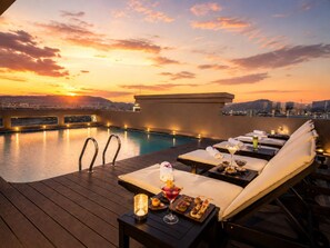 Un espace piscine sur le toit, avec des chaises longues, une table de bar où sont servis des boissons et des en-cas, et une vue imprenable sur le coucher du soleil.