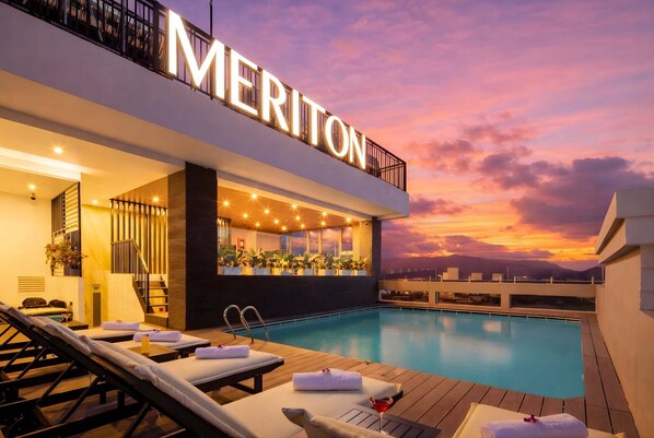 Un hôtel doté d’une piscine sur le toit, de chaises longues et d’un espace bar.