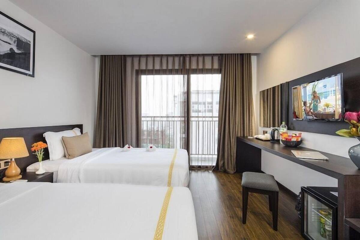 Une chambre d’hôtel avec deux lits, un bureau, une chaise, une télévision et une fenêtre avec des rideaux.