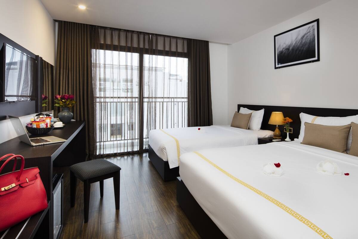 Une chambre d’hôtel avec deux lits, un bureau avec un ordinateur portable, un sac à main rouge et une fenêtre avec des rideaux.