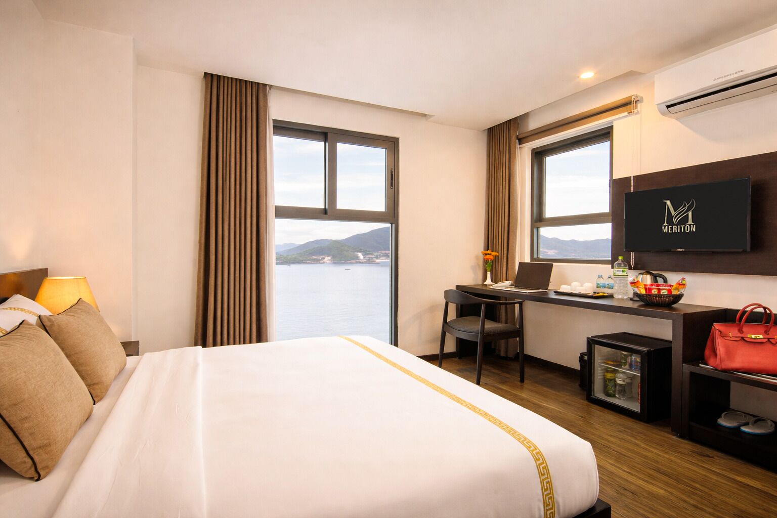 Habitación de hotel con cama, escritorio, silla, televisor y vista al mar.